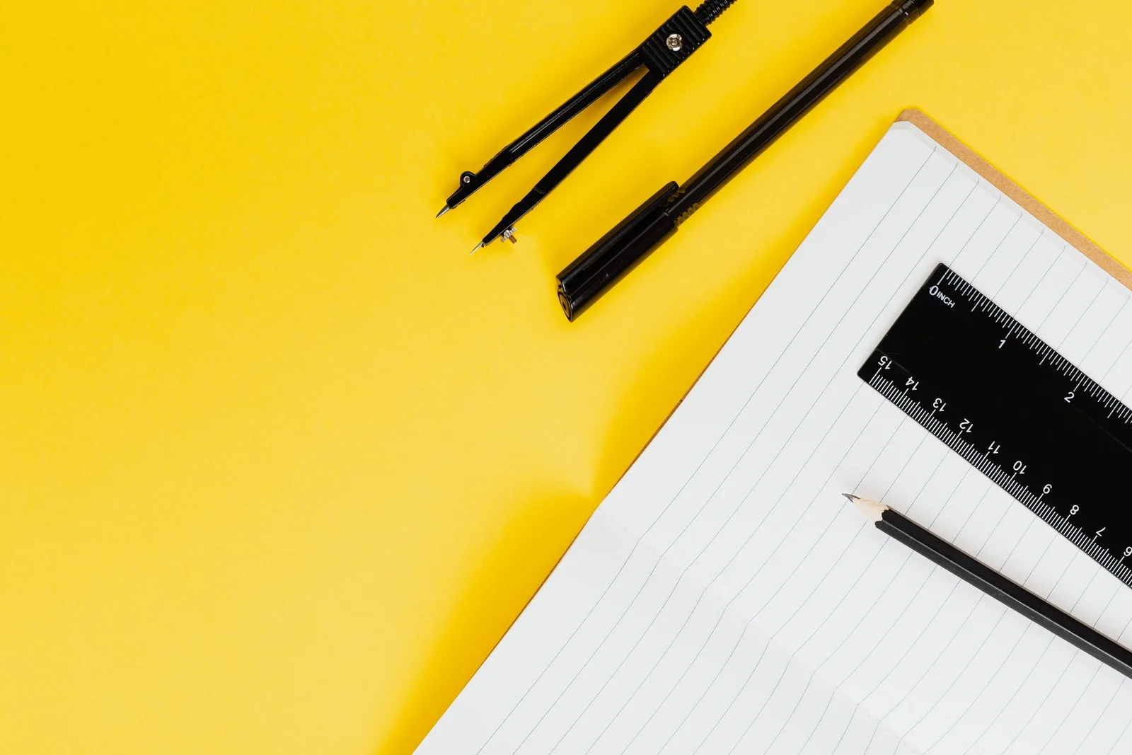 A compass, pen, ruler and notebook on a yellow desk