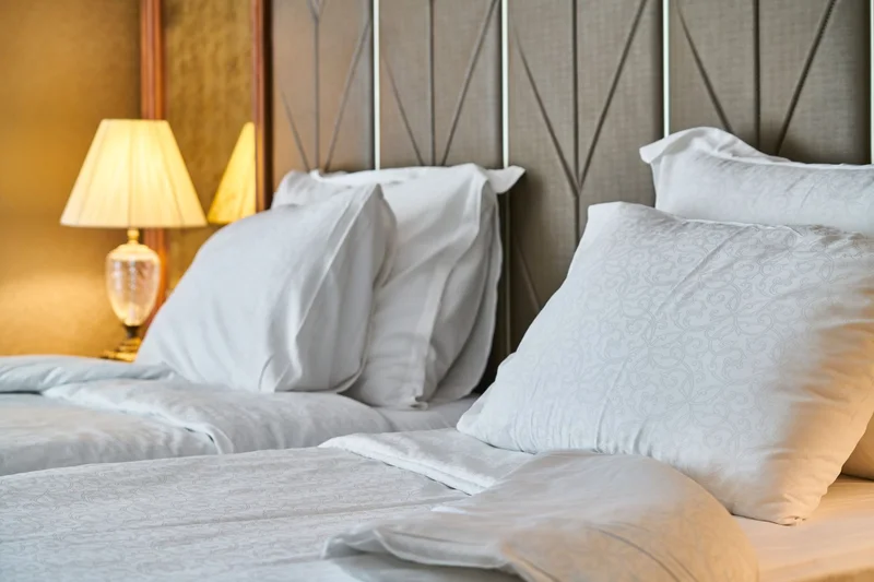 A bed with white pillows beside a lit lamp