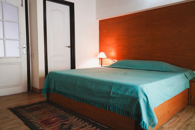 A simple bedroom with a teal bedspread and a lamp