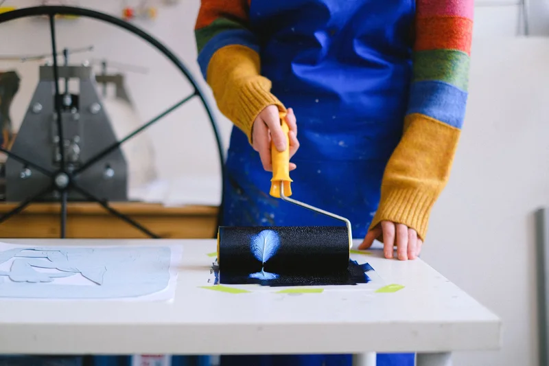 A person in an apron inking a printing plate