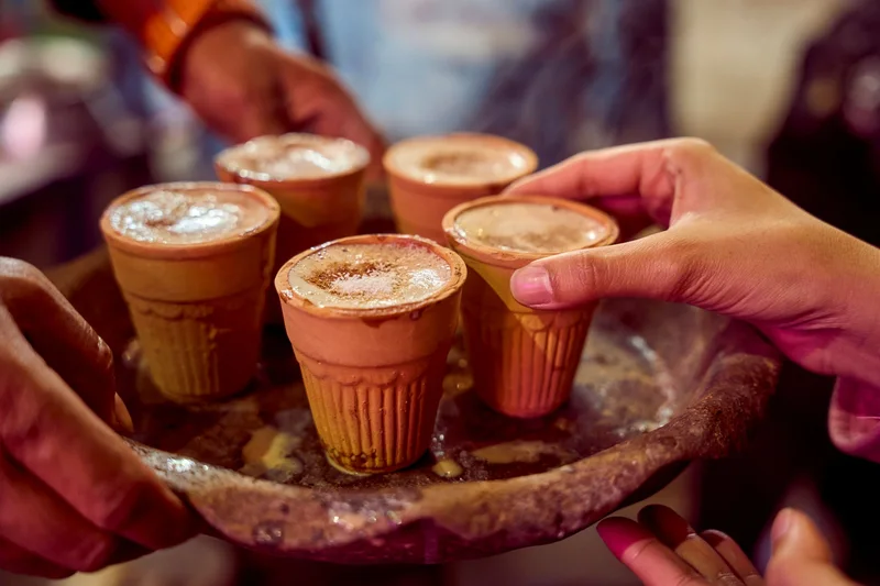 Hands passing a tray of masala chai in clay cups