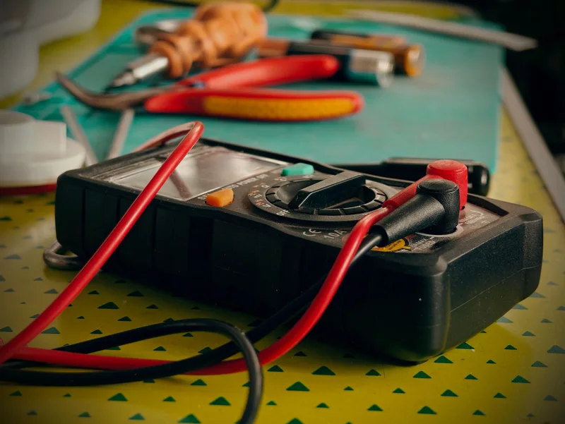 A multimeter and pliers on a workbench